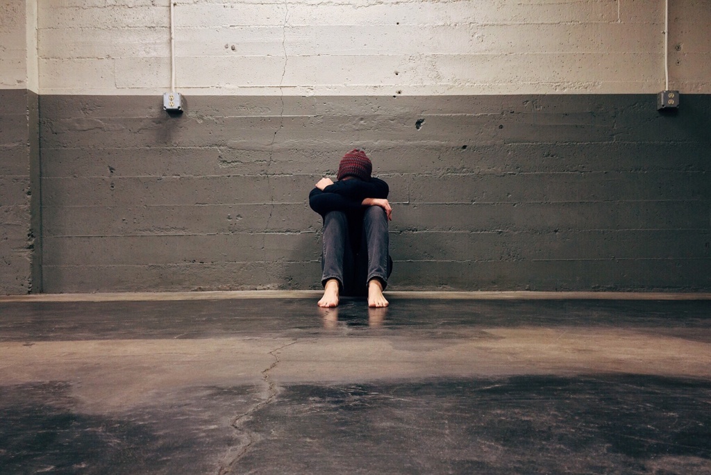 Teen boy sitting against a wall with hands holding his head